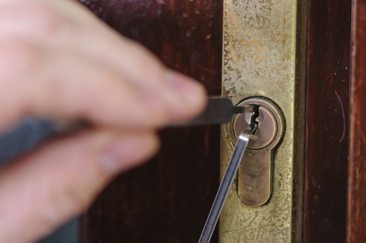 A man uses lockpicking tools to pick the lock of a house.